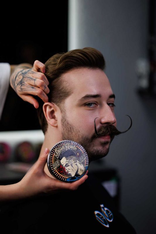 Укладка волосся та вусів із використанням стайлінгу Bad Groom Scissor Hands у барбершопі.